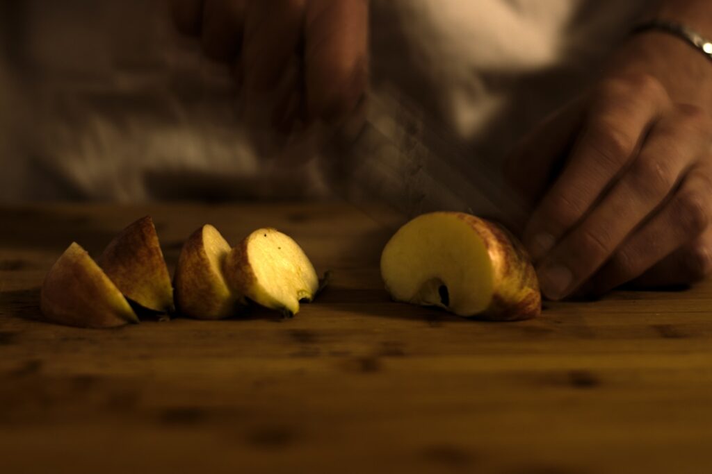 Person cutting an apple in a blurry motion on a chopping board made of wood, with apple quarters on the side.